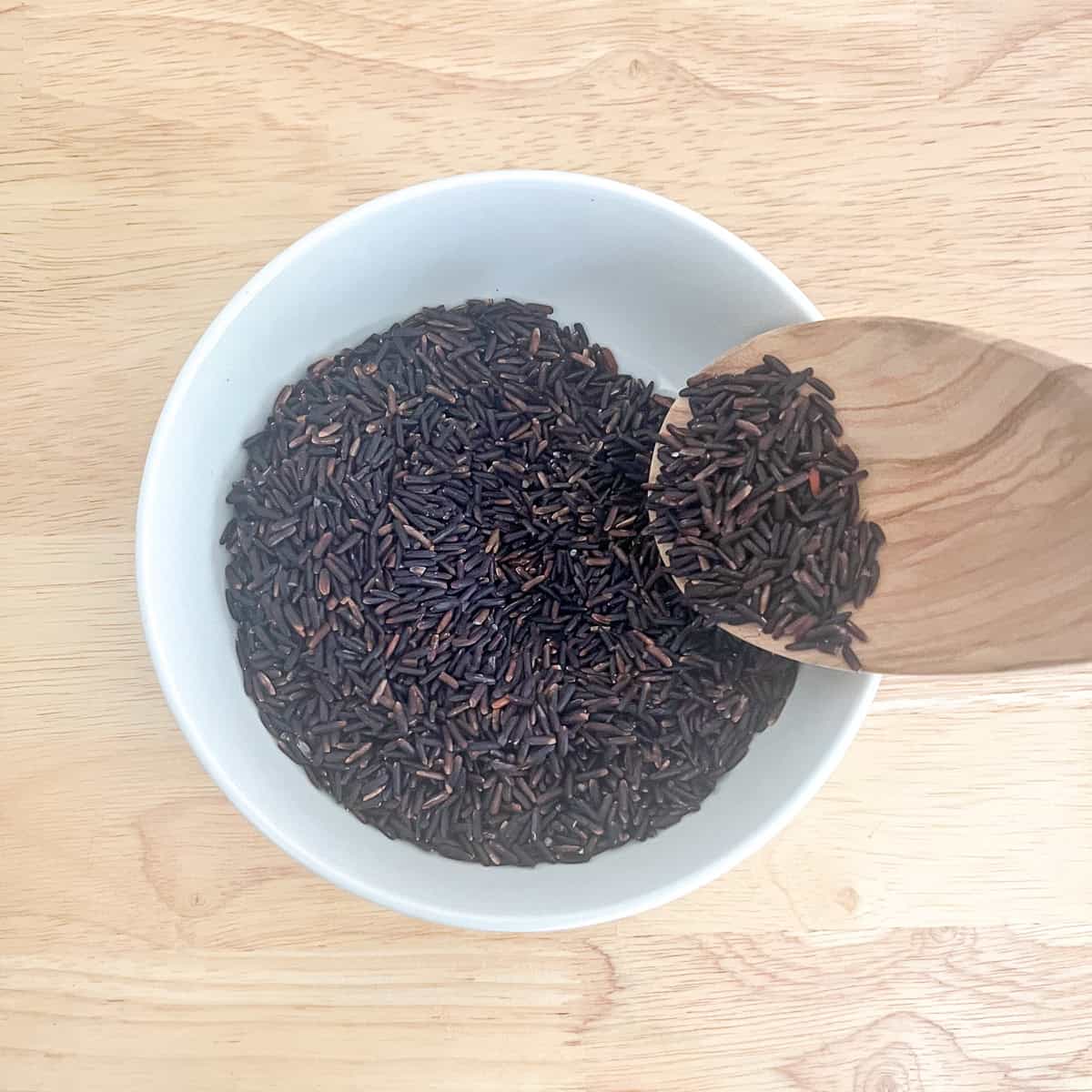 Dry black rice in a bowl with wooden spoon to show rice texture.