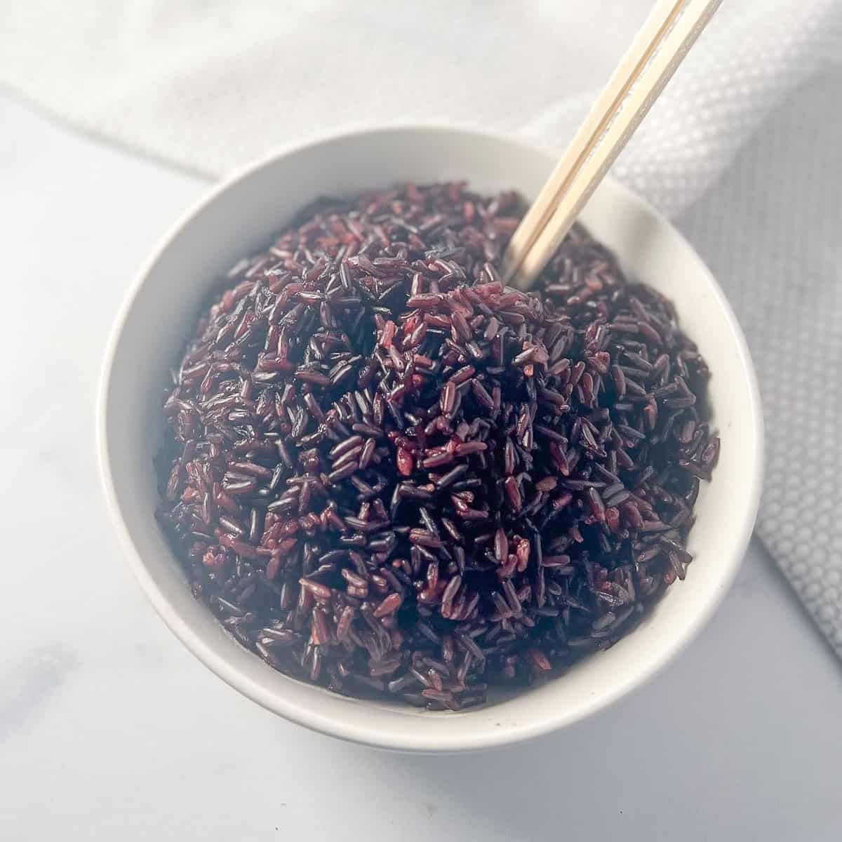 Cooked black rice in a bowl with chopsticks.