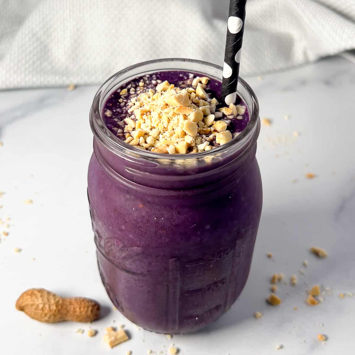 Blueberry peanut butter smoothie in a mason jar with straw.