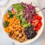 Nourish bowl with tempeh, butternut squash, black rice, red bell pepper, purple cabbage, cilantro and kale; topped with peanut sauce.