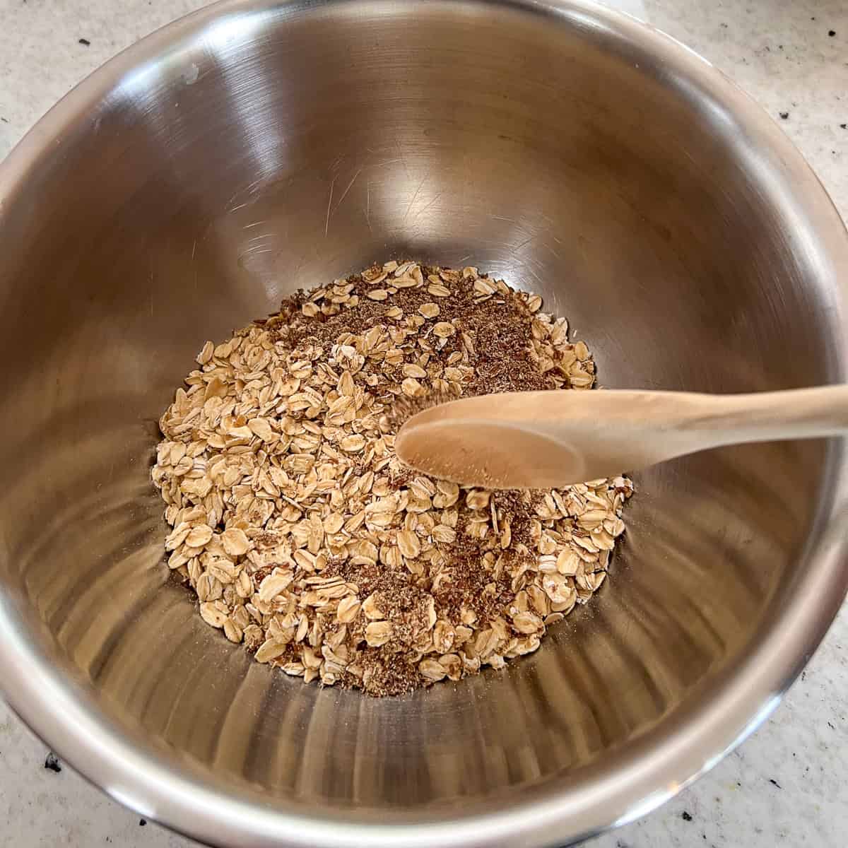 Rolled oats being combined in a mixing bowl with ground flaxseeds.