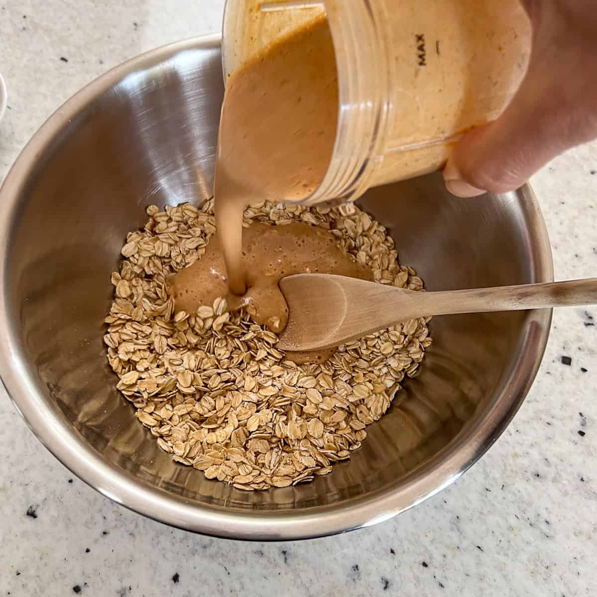 Pumpkin mixture being added to a mixing bowl with rolled oats and ground flaxseeds.