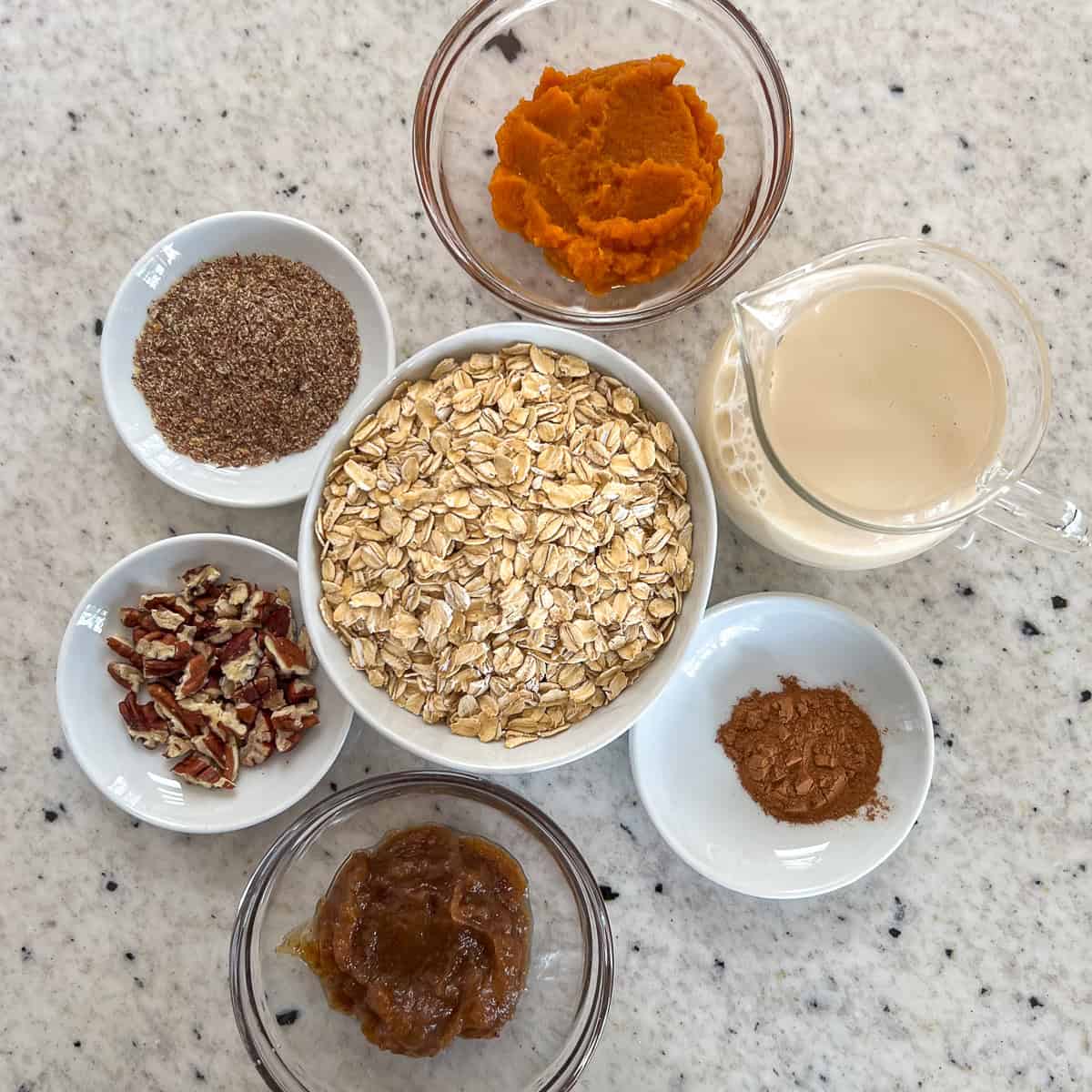 Ingredients for pumpkin spice overnight oats: rolled oats, pumpkin puree, ground flaxseeds, date syrup, pumpkin spice, plant based milk, and pecans.