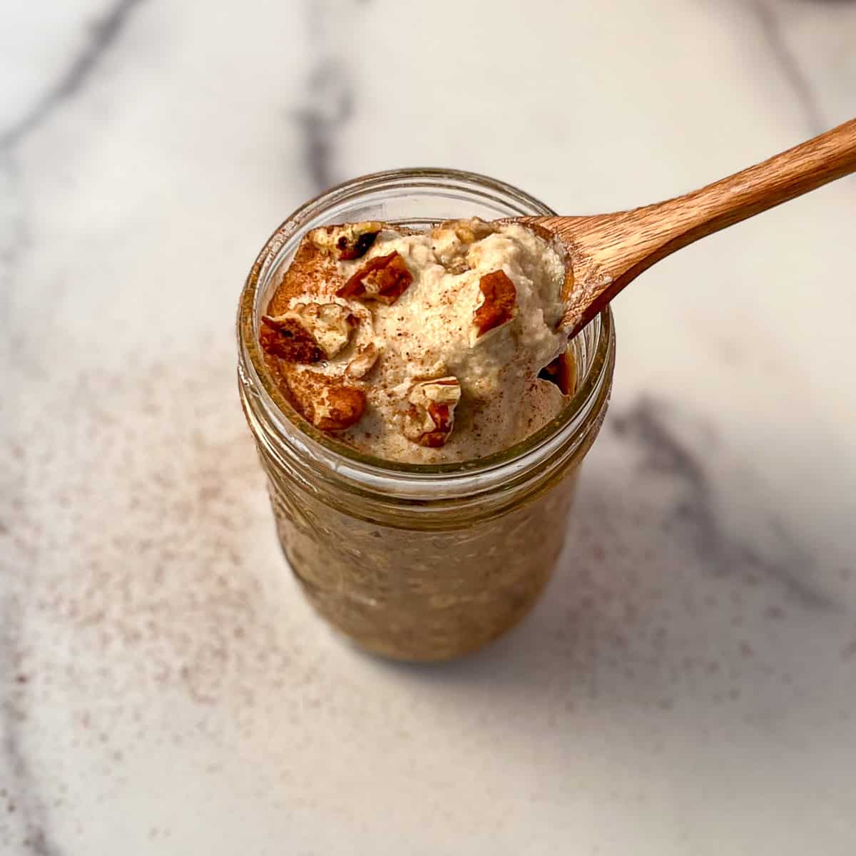 Pumpkin spice overnight oats in a mason jar topped with sweet cashew cream and chopped nuts and wooden spoon.