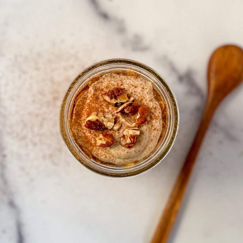 Top view of overnight oats topped with chopped nuts and sweet cashew cream in a mason jar with wooden spoon on the side.