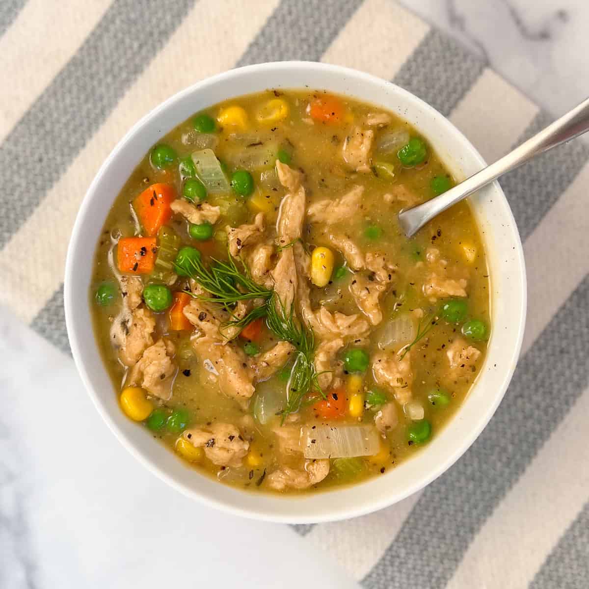 A bowl of vegan chicken vegetable soup with a spoon.