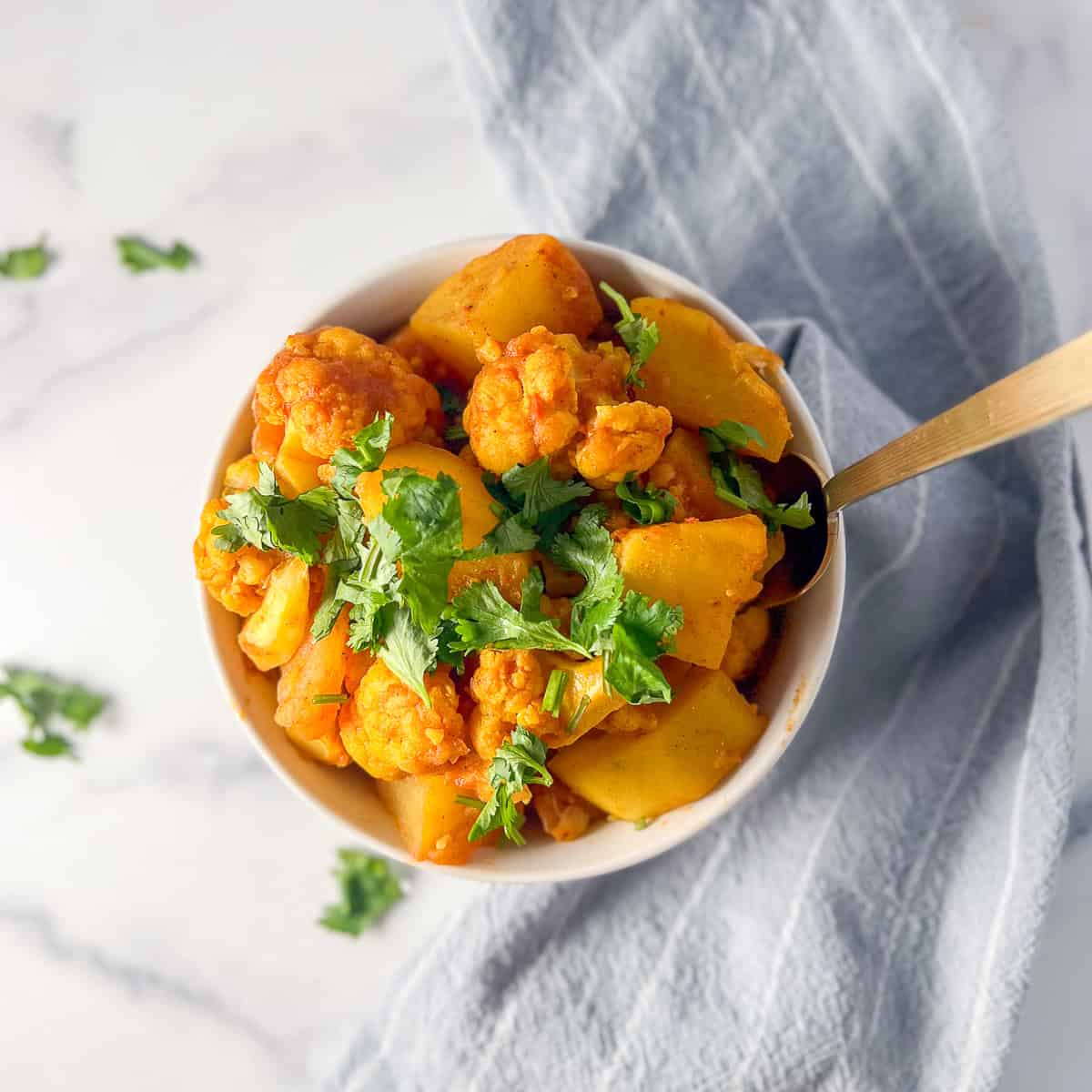 A bowl of aloo gobi potatoes and cauliflower with a spoon.