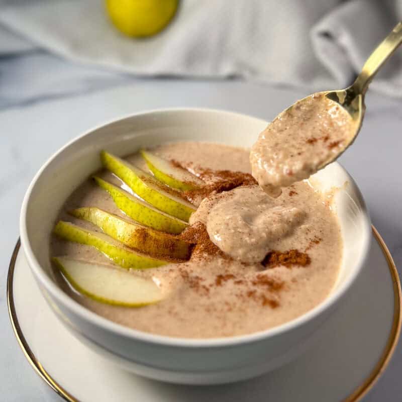 A bowl of millet porridge topped with sliced pear and cinnamon, and a spoon coming out of the bowl.