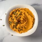 Savory pumpkin hummus in a bowl topped with pumpkin seeds.
