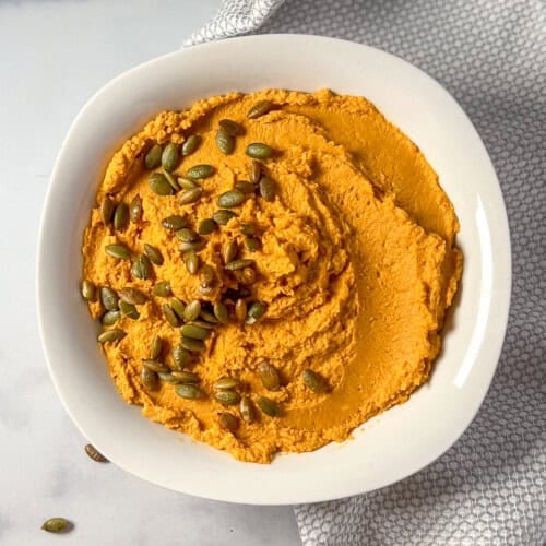A bowl of pumpkin hummus topped with pepitas.