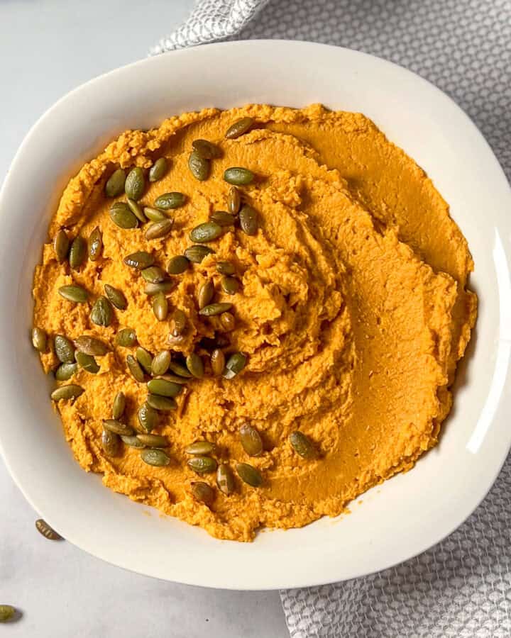 A bowl of pumpkin hummus topped with pepitas.