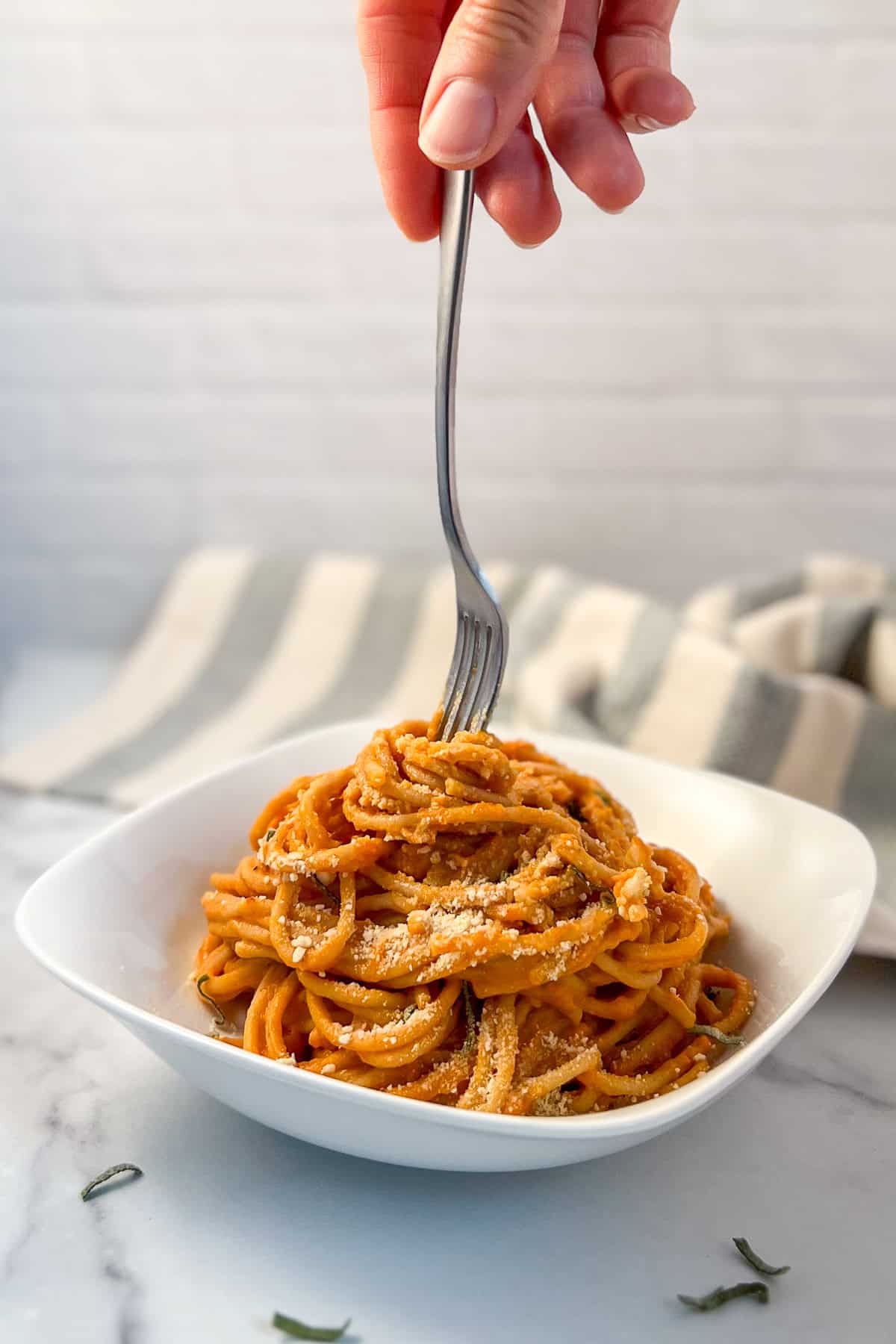 A bowl of creamy pumpkin pasta with a woman's hand twirling pasta around a fork.