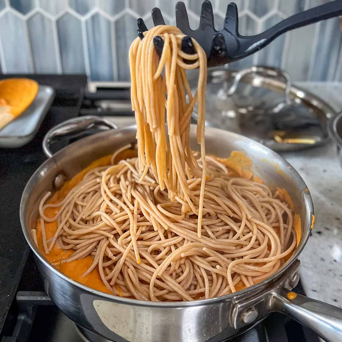 Cooked pasta being added to the skillet with the creamy vegan pumpkin sauce.