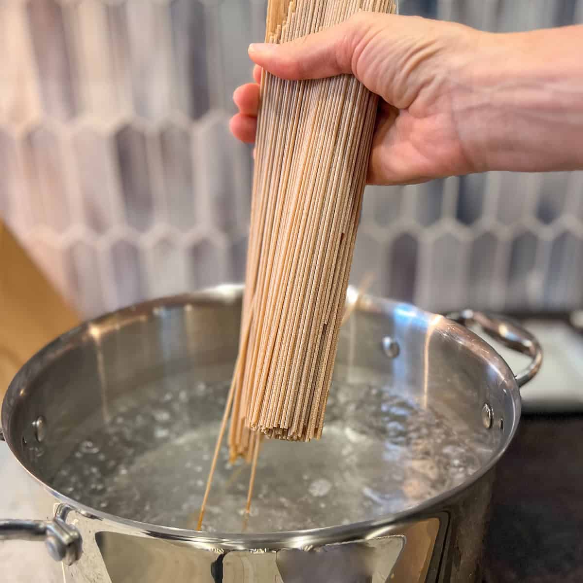 Spaghetti being added to a pot of boiling water on the stovetop.