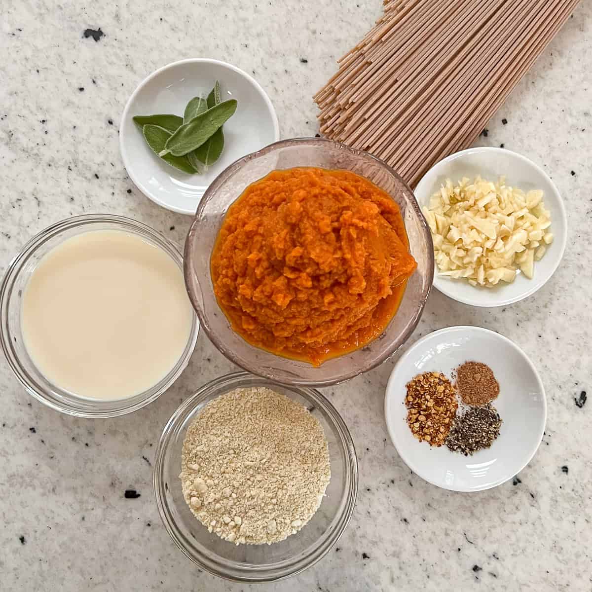 Ingredients for pumpkin pasta: pumpkin puree, garlic, soymilk, spices, whole grain pasta, cashew parmesan cheese and fresh sage.