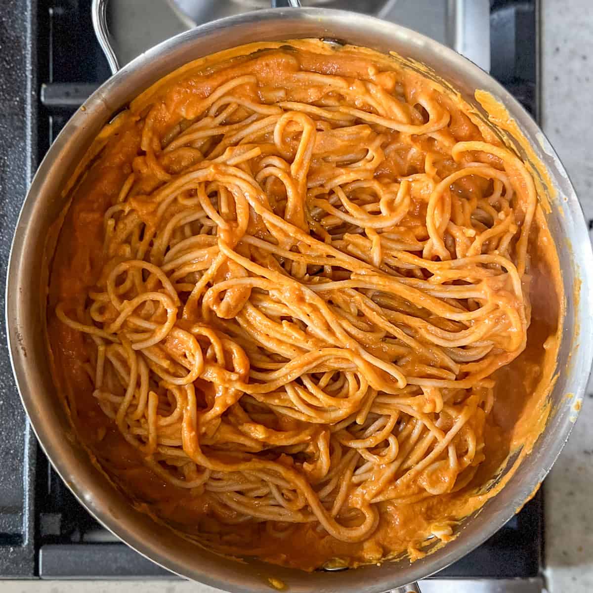 Skillet with creamy vegan pumpkin pasta with sauce coating the spaghetti pasta.