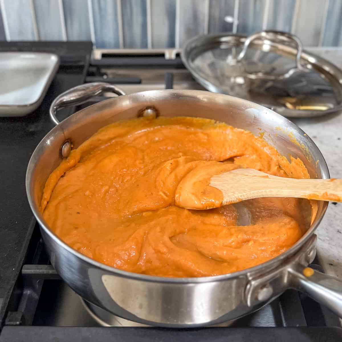 Creamy pumpkin pasta sauce being stirred in the skillet with a wooden spoon.