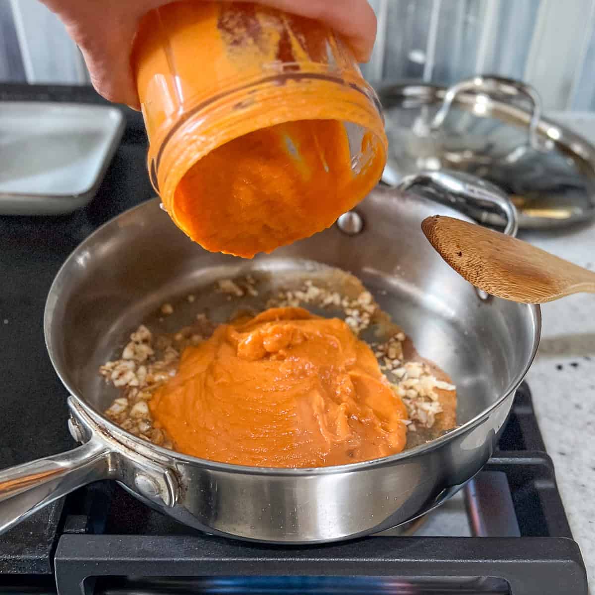 Pumpkin sauce mixture being added to the skillet with sautéed garlic and spices.