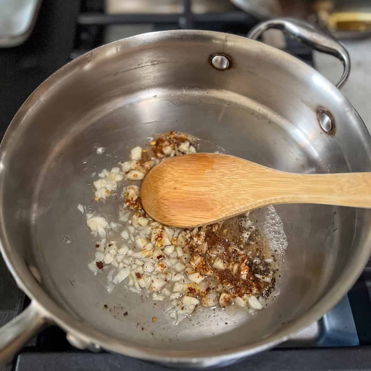 Garlic and spices being stirred in the skillet with a wooden spoon.