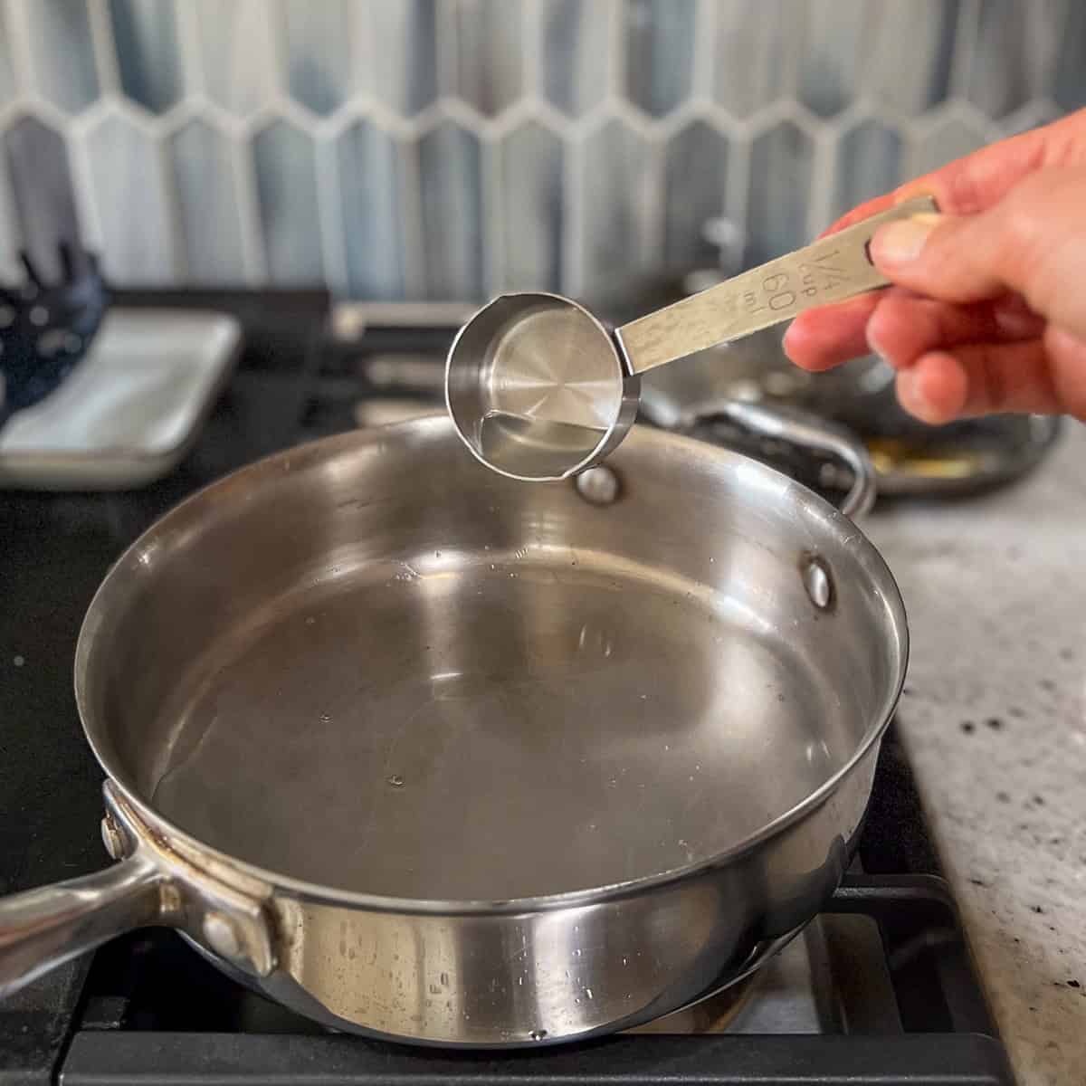 Pasta water being added to a large skillet to cook garlic and spices.