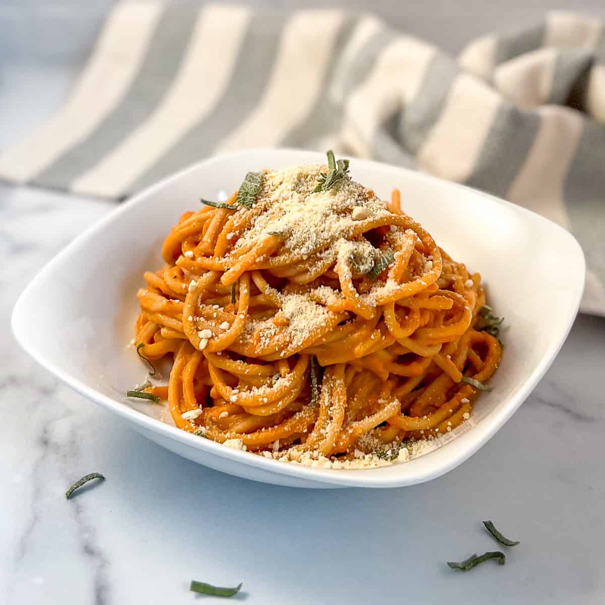 Creamy vegan pumpkin pasta in a bowl topped with fresh chopped sage and cashew parmesan cheese. 