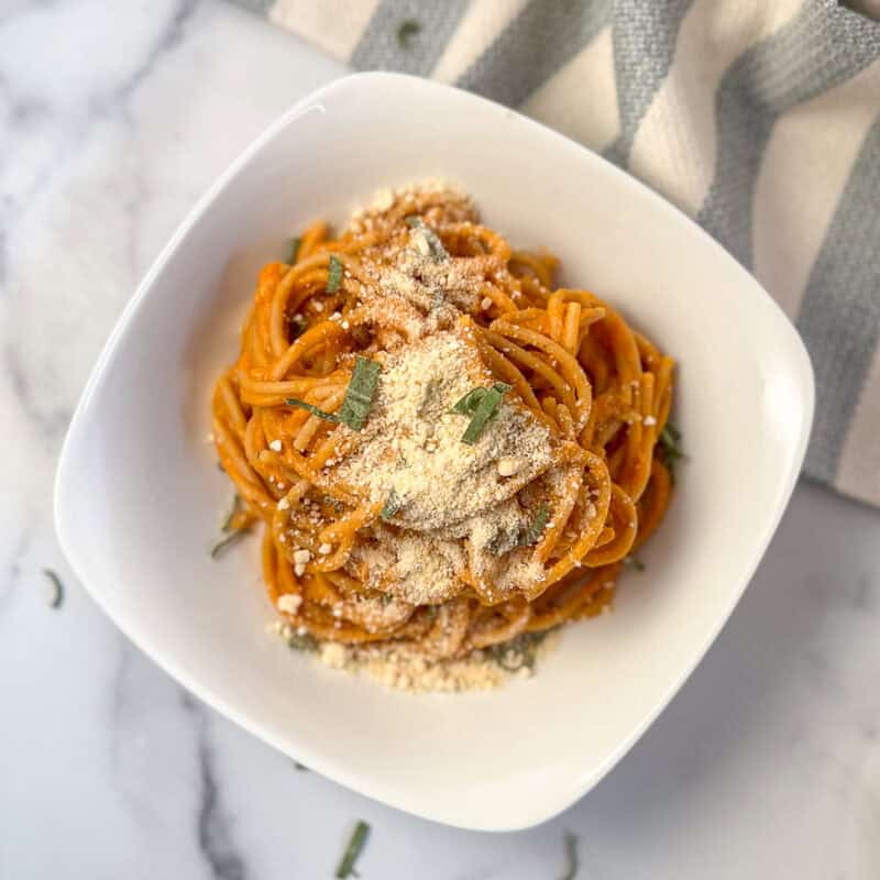 Top view of a bowl of pumpkin pasta topped with chopped sage and vegan cashew parmesan cheese.