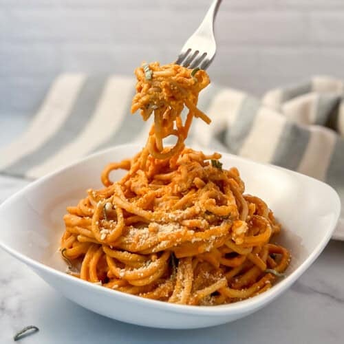 Creamy vegan pumpkin pasta in a bowl with a fork lifting some out.