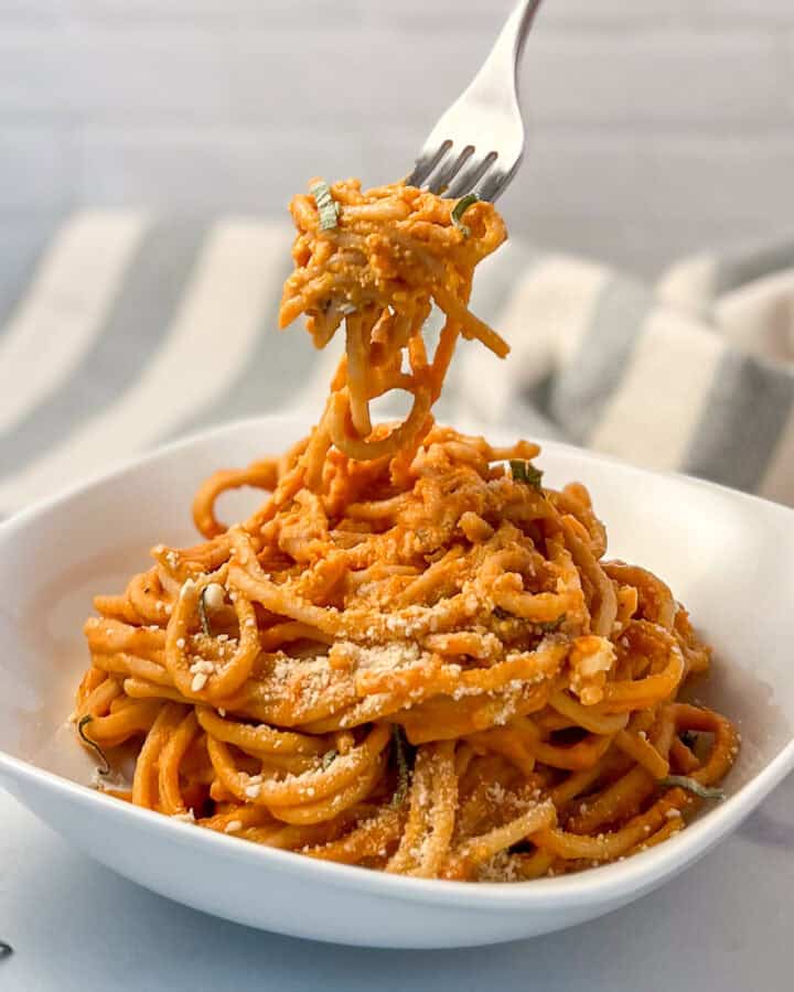 Creamy vegan pumpkin pasta in a bowl with a fork lifting some out.
