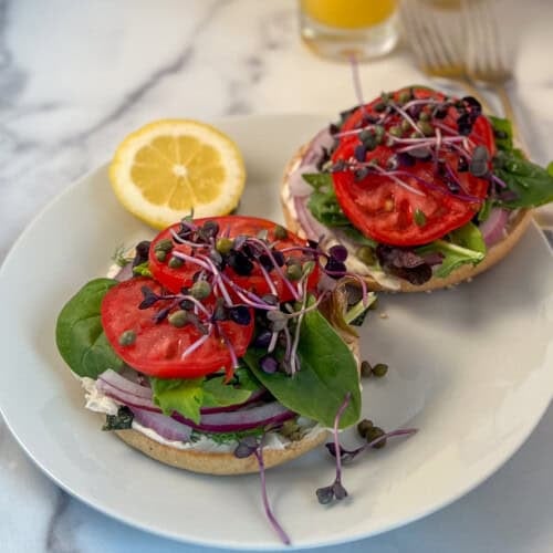 Garden veggie bagel halves on a plate with lemon wedge.