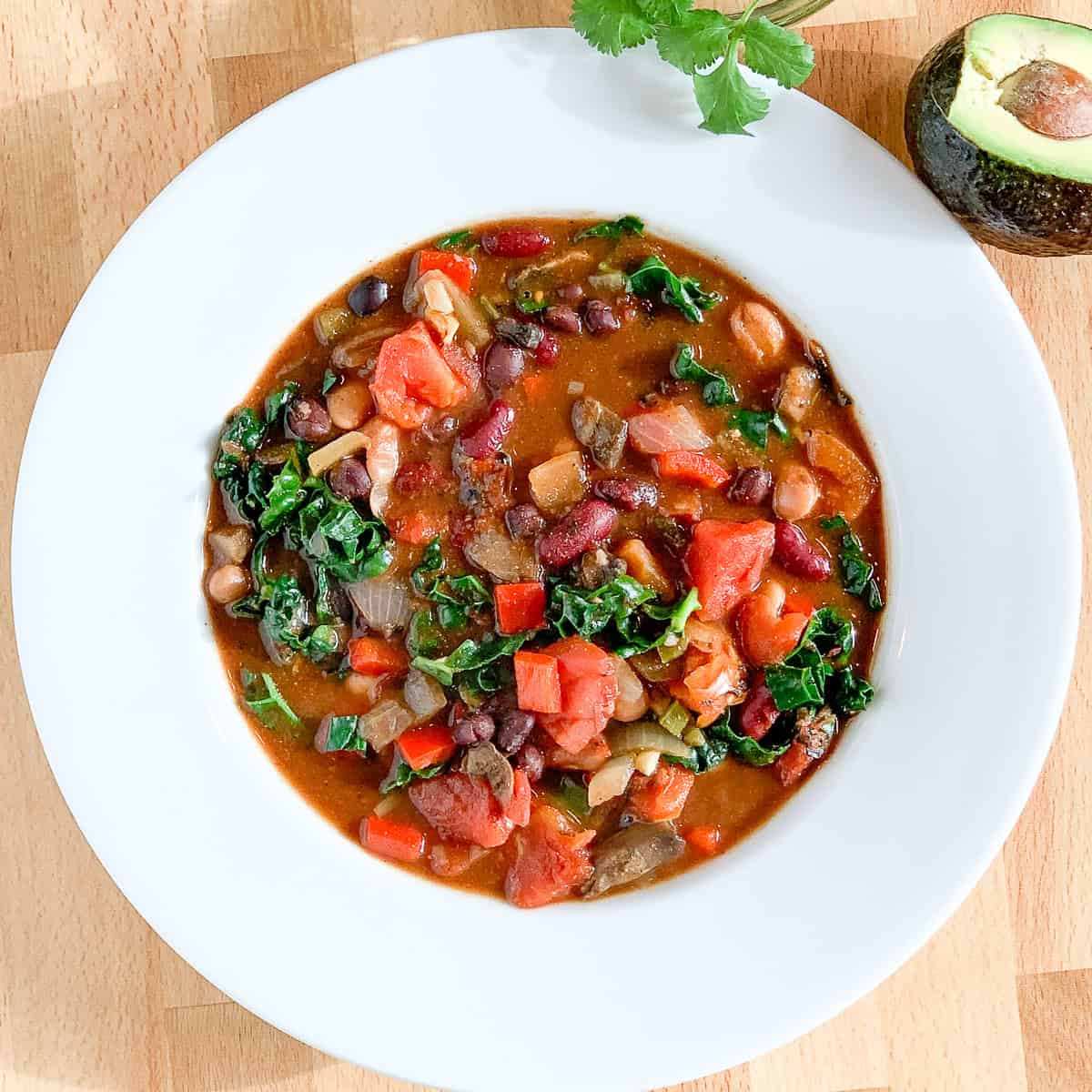 A bowl of veggie chili with avocado and cilantro on the side.