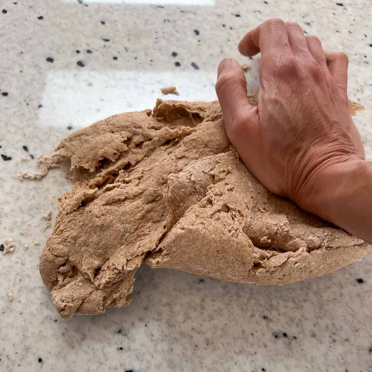 A woman's hand kneading the dough on the countertop.