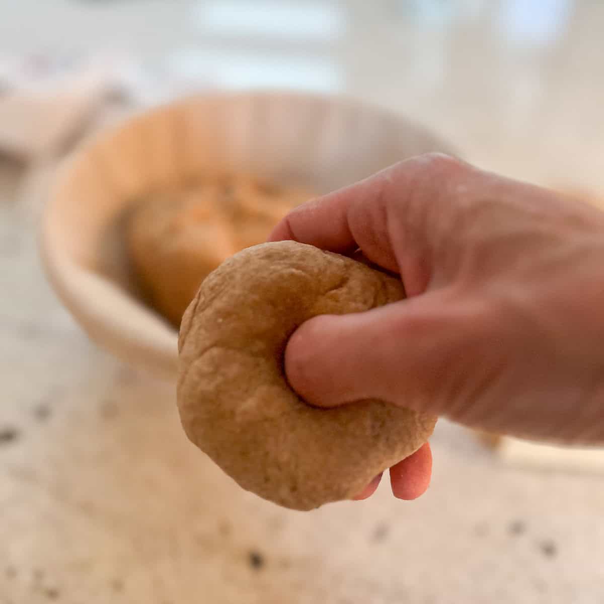 Dough that is being shaped by a woman's hand with her thumb punching a whole in the middle of the dough.