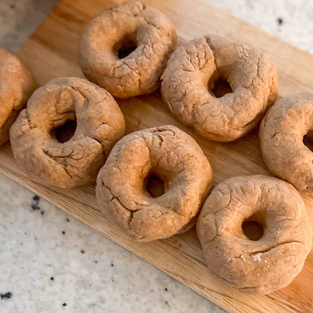 Uncooked bagels arranged on a cutting board ready for boiling.