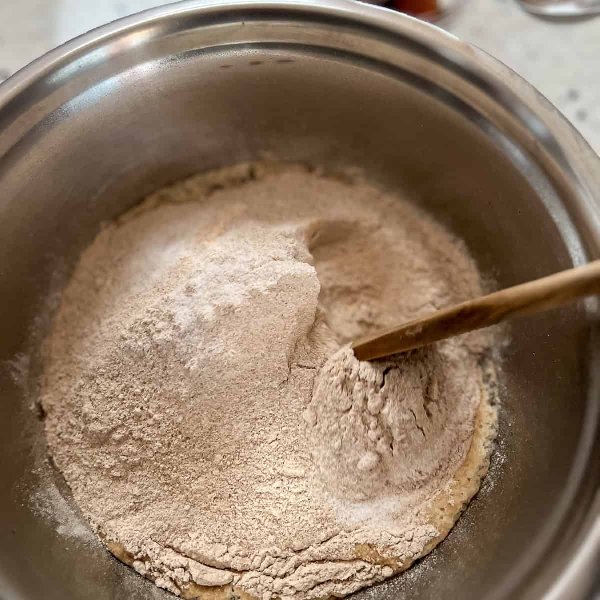 A wooden spoon mixing the flour and yeast mixture together in a large mixing bowl.