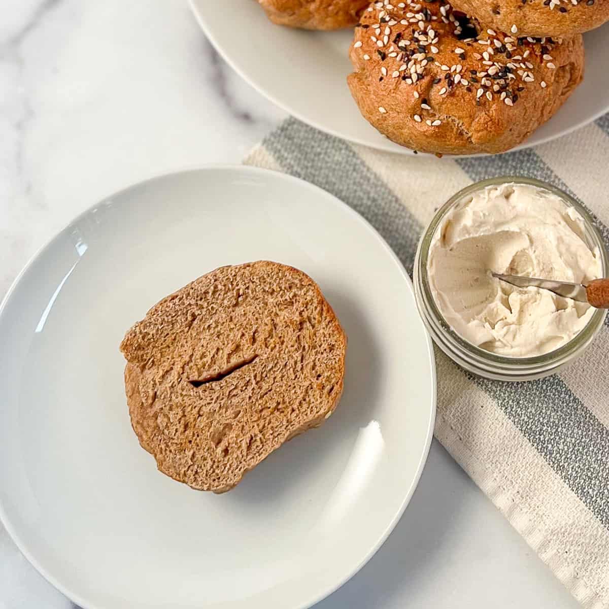 Half of a toasted whole wheat bagel on a plate with homemade cashew vegan cream cheese on the side.