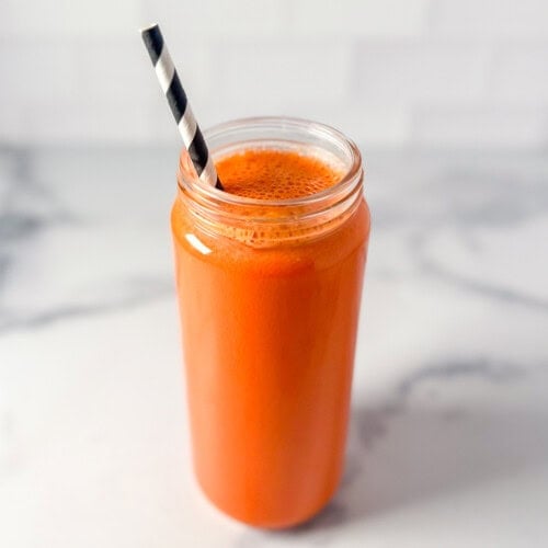 Carrot and ginger juice in a tall juice container with a straw.