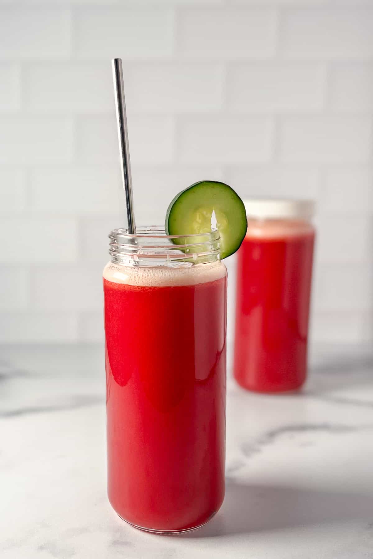 A tall glass of cabbage and pineapple juice with a straw and sliced cucumber garnish.