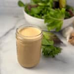 A mason jar with cashew butter sauce and salad greens in the background.