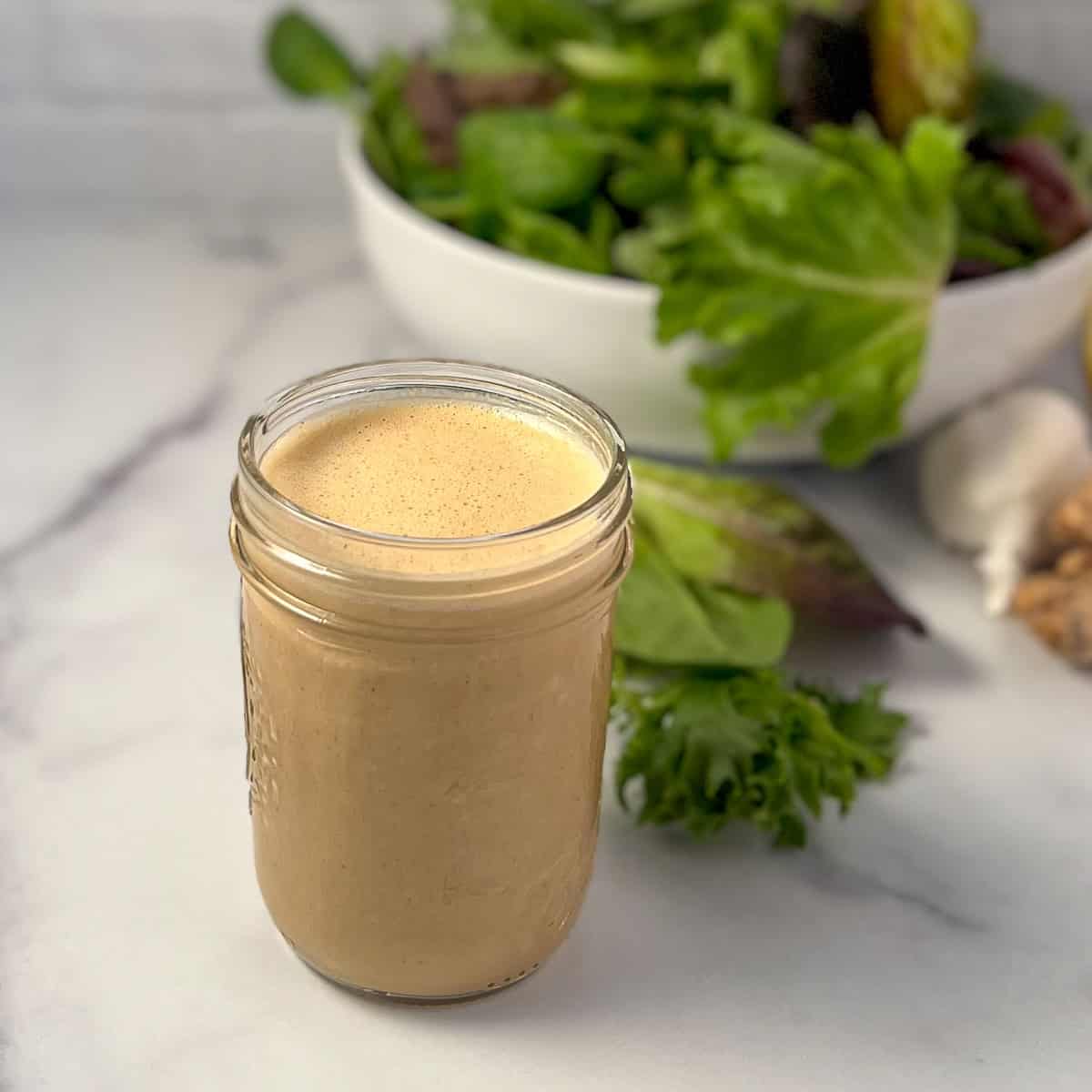 A mason jar with cashew butter sauce and salad greens in the background.