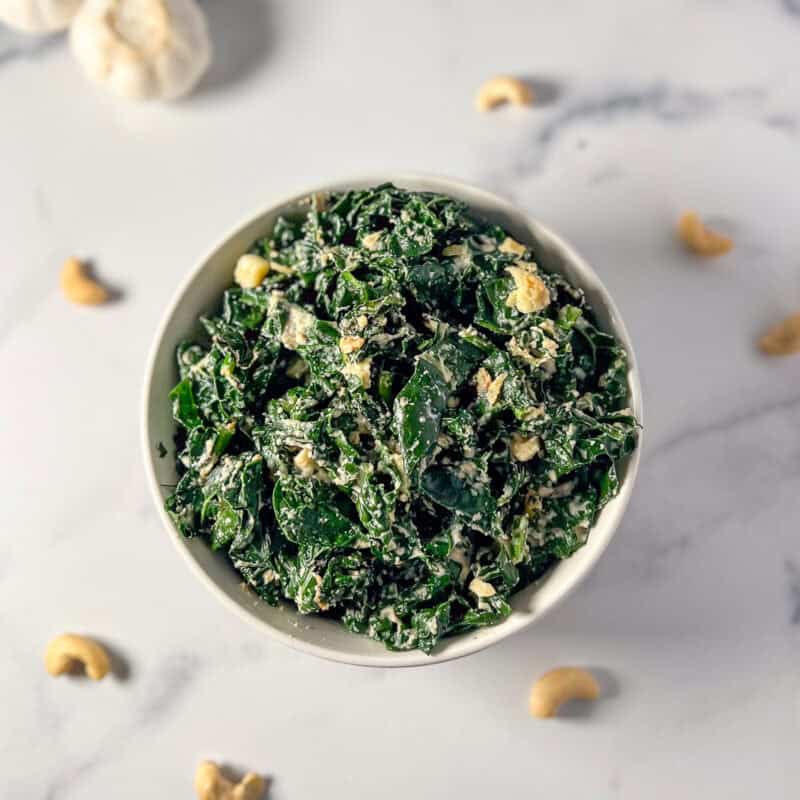 A bowl of garlicky kale with loose cashews in the background.