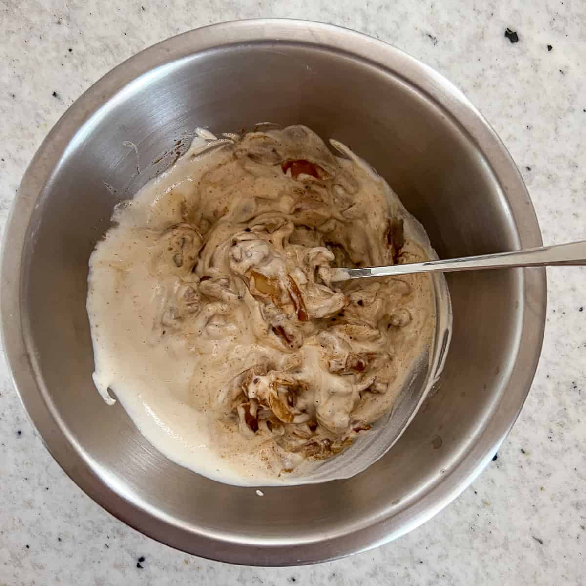 Vegan french onion dip in a mixing bowl with a spoon for stirring to combine ingredients.