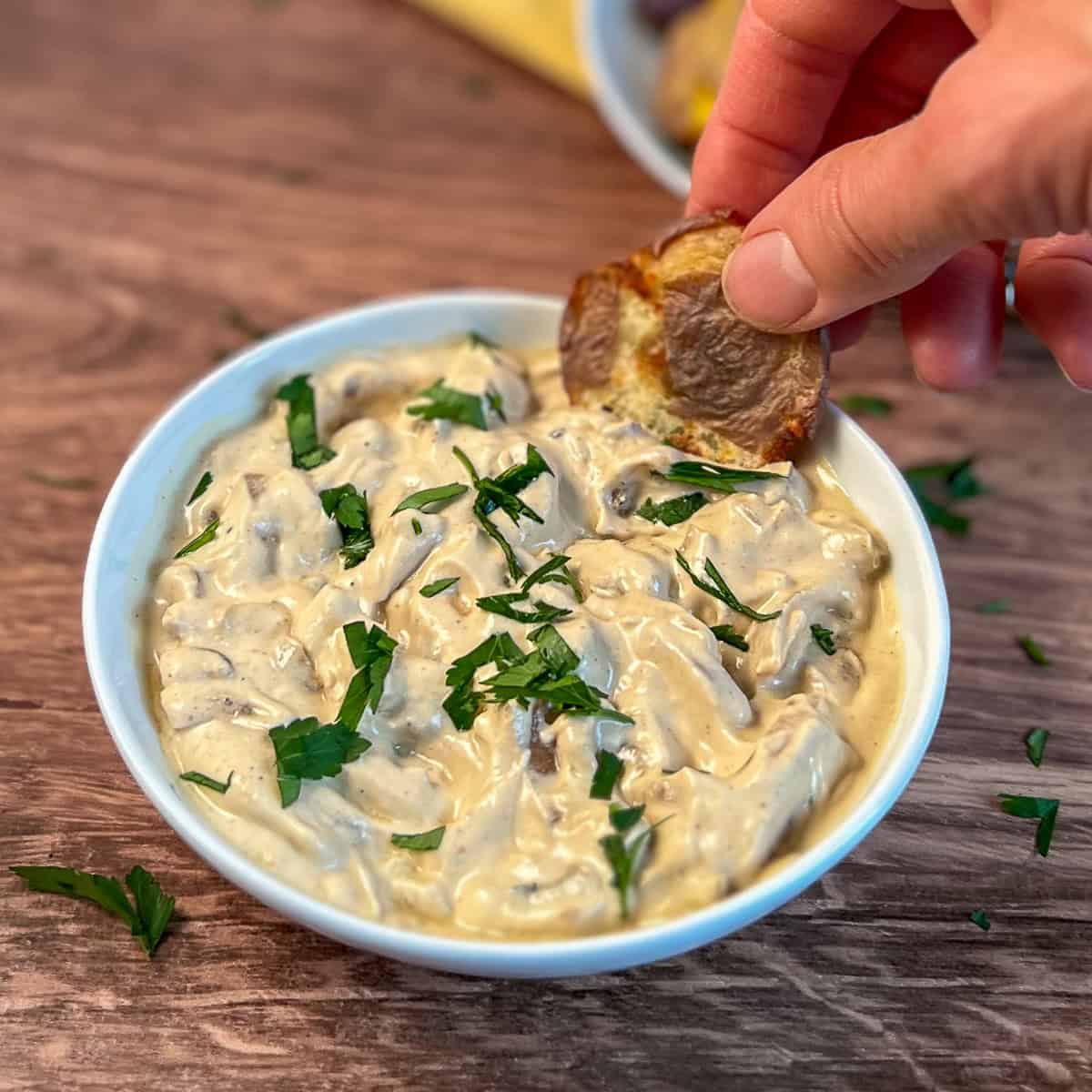 Vegan French onion dip in a bowl with a woman's hand taking an air fryer smashed potato to dip.