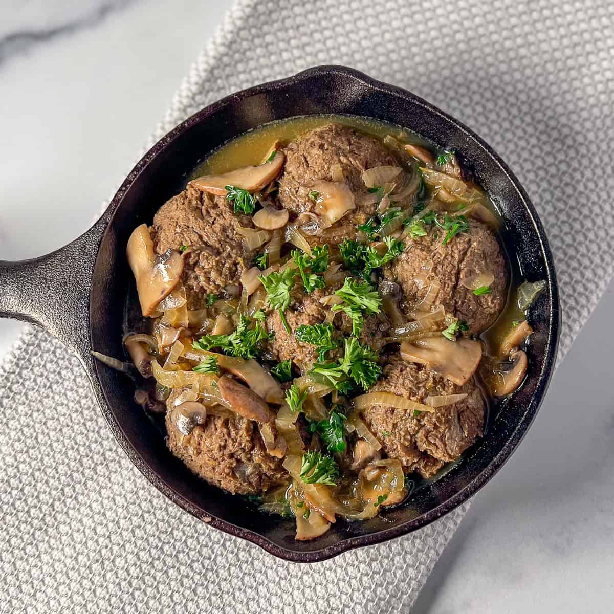 Vegan Swedish meatballs in a cast iron skillet with mushroom gravy and topped with fresh chopped parsley.