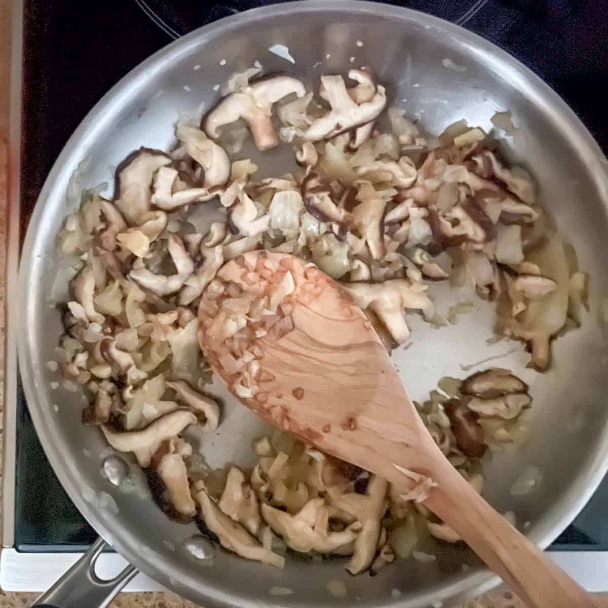 Sautéed mushrooms and onions in a skillet with wooden cooking spoon.