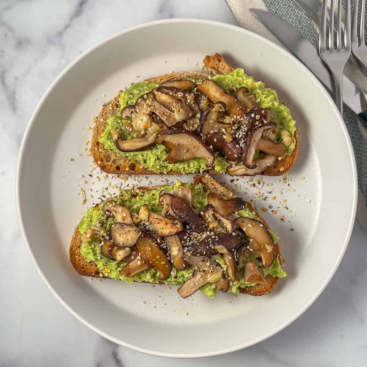 Two slices of avocado toast topped with sautéed mushrooms and garlic.