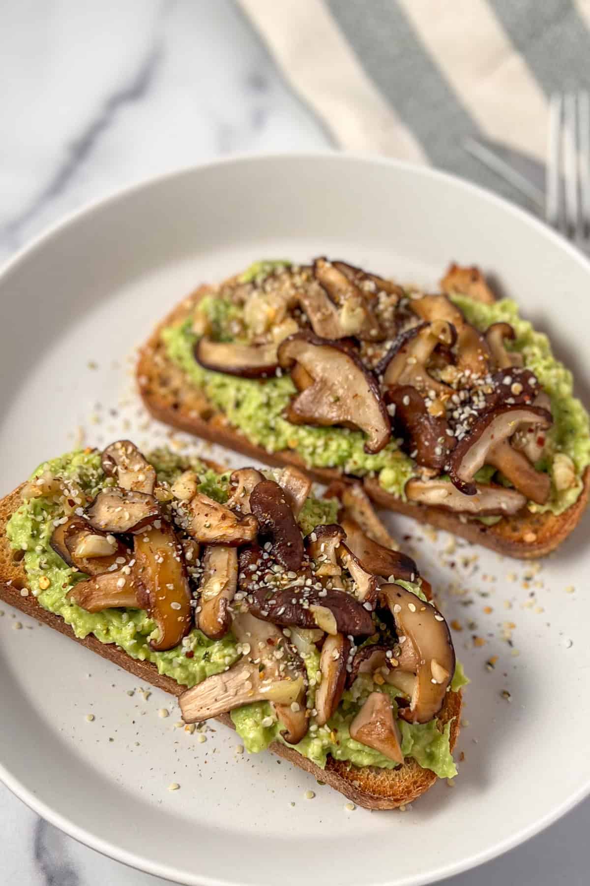 Two pieces of avocado toast topped with sautéed mushrooms and garlic.