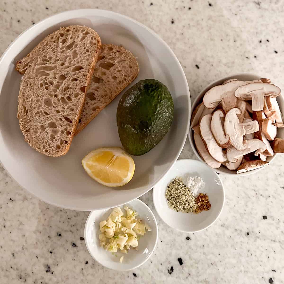 Ingredients for avocado toast: sourdough bread, avocado, lemon, mushrooms, garlic, hemp hearts, salt and crushed red pepper flakes.