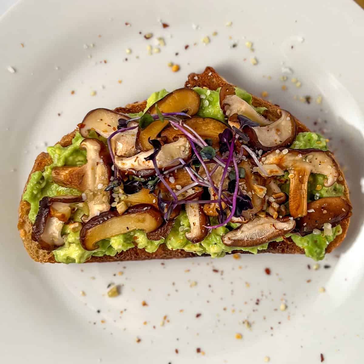 Avocado toast with sauteed mushrooms and garlic and topped with hemp hearts, microgreens, course salt, and crushed red pepper flakes.