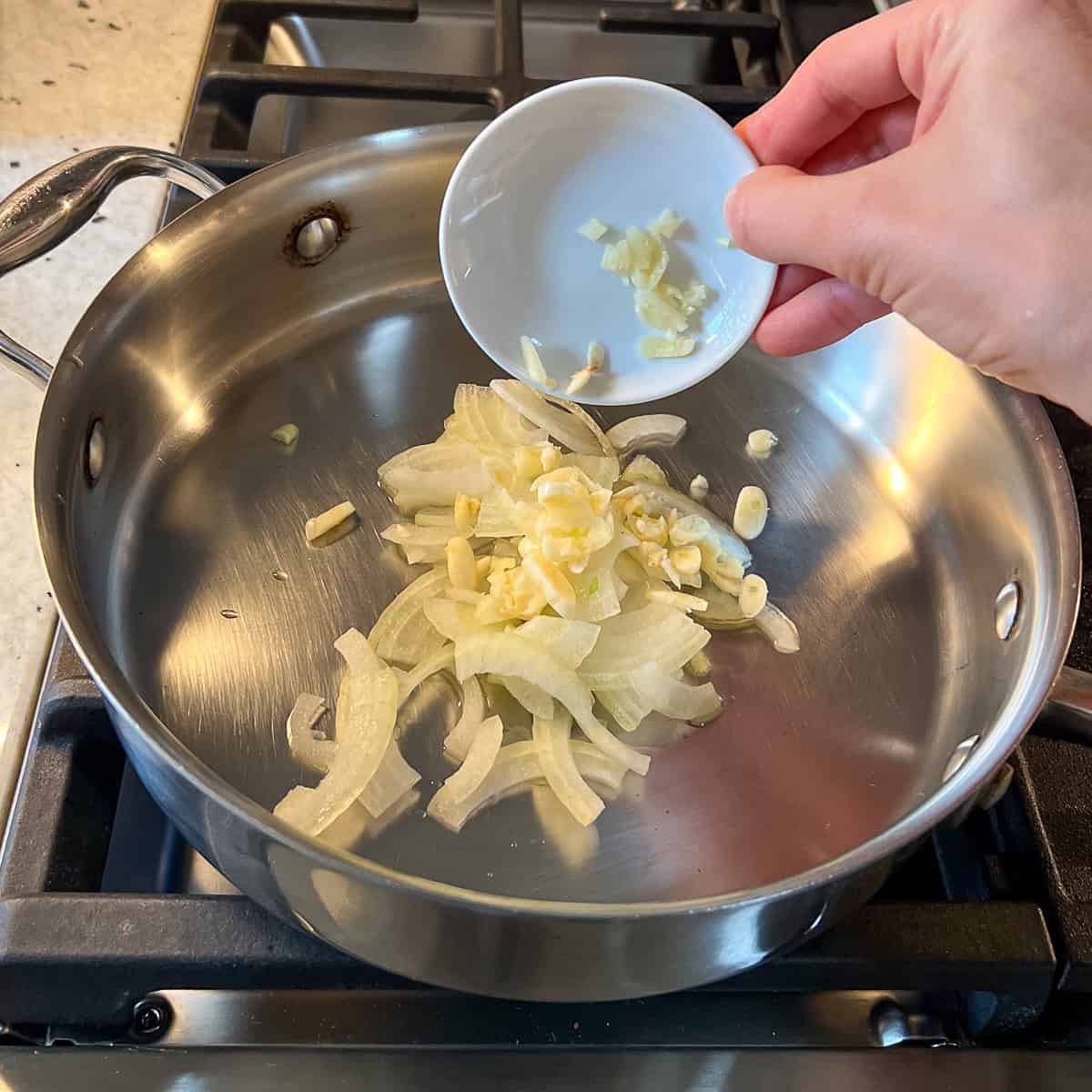 Onion and garlic being added to a heated skillet.