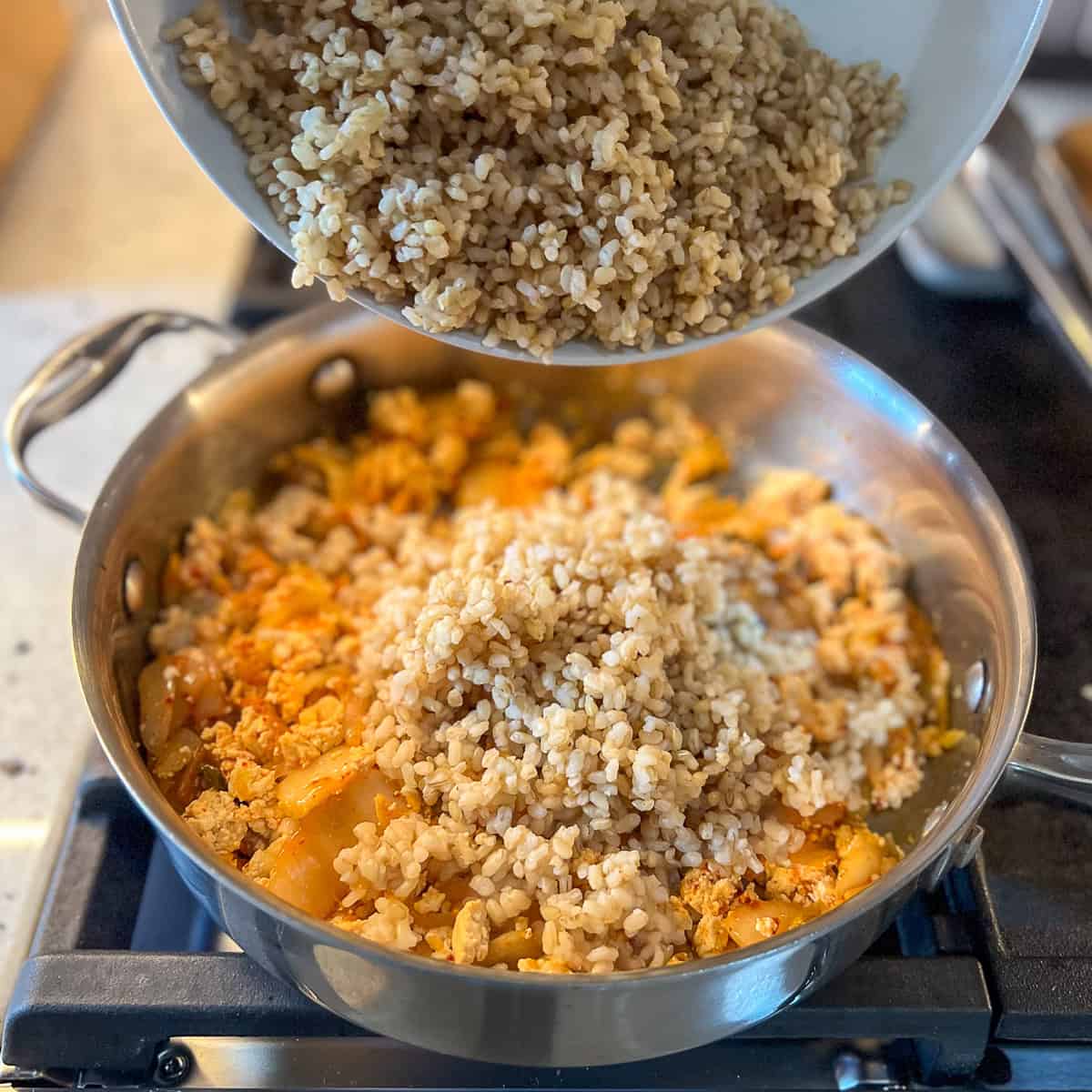 Brown rice being added to the pan with tofu and veggies.